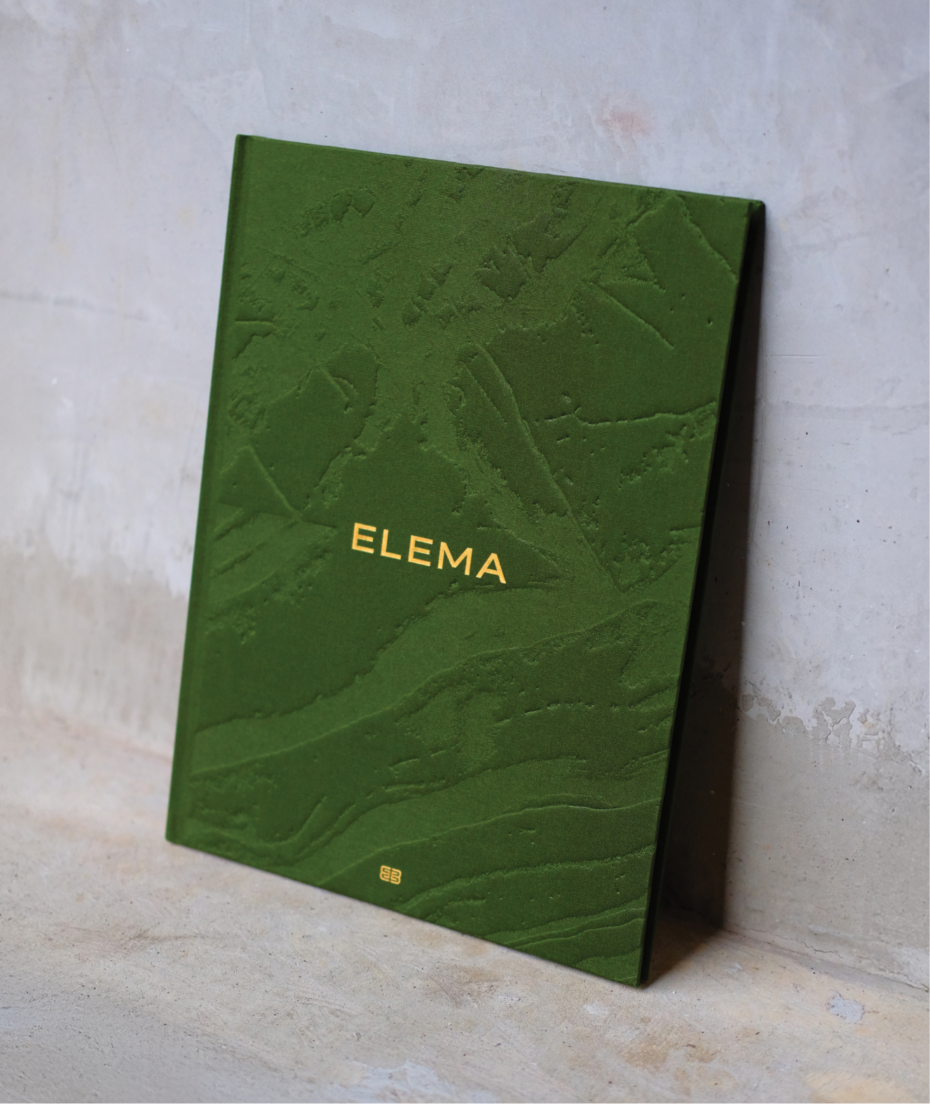 A green, textured hardback book titled ELEMA in gold lettering, used for a personalised property marketing campaign, with a small gold logo at the bottom.