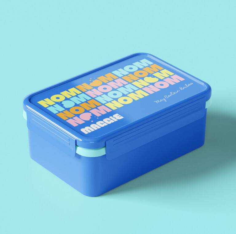 Blue plastic lunchbox with the repeated text NOM in yellow and orange on the lid, personalised with the name Maggie and the phrase May Contain Bribes, showcasing a personalised property marketing campaign adapting in real time.