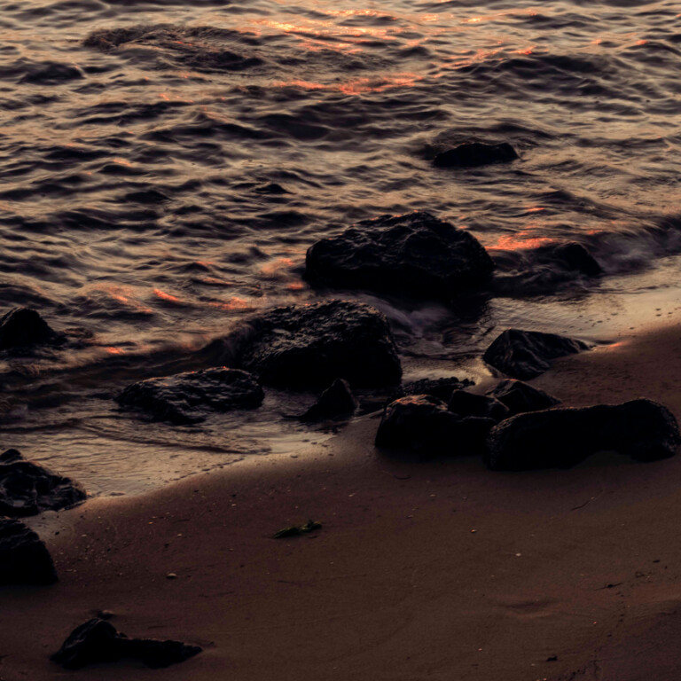 Dark rocks on a sandy beach meet the edge of the ocean at sunset, reflecting a personalised property marketing campaign adapting in real-time.
