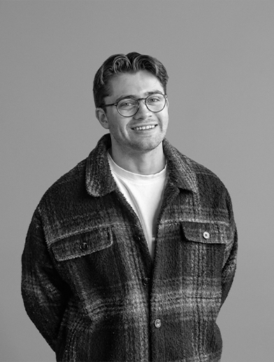 A smiling young man wearing glasses and a checked collared jacket.